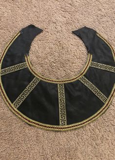 a black and gold bib laying on top of a carpeted floor next to a pair of scissors