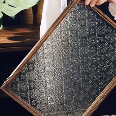 a person holding up a framed piece of metal