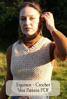 a woman wearing a brown sweater and jeans is holding her hair in one hand while looking at the camera