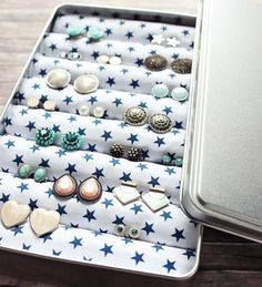 an open tin with several pairs of earring and studs in it on a wooden table