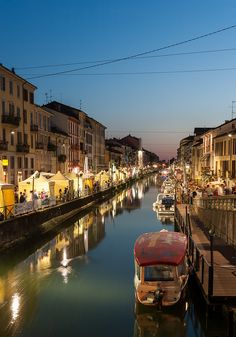 boats are parked along the side of a river at night in an urban area with buildings on both sides