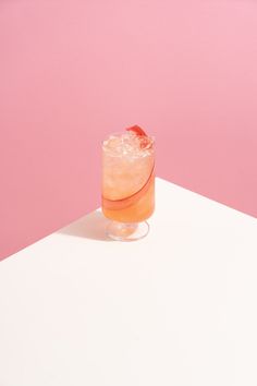 a drink sitting on top of a white table next to a pink and white wall