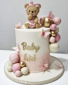 a pink and gold baby shower cake with a teddy bear sitting on top of it