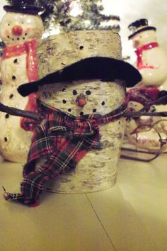 there is a snowman made out of birch tree trunks and wearing a black hat