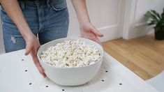 a person holding a bowl of popcorn on top of a table