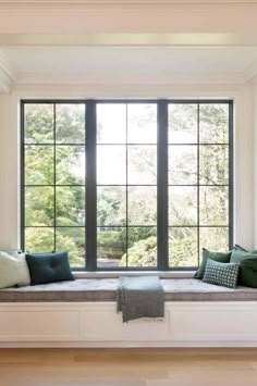 a window seat with pillows and blankets on it in front of a large windowsill