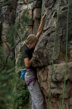 a woman climbing up the side of a rock with her hands in the air while holding on to ropes