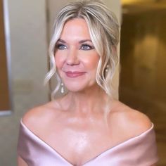 a woman with blonde hair and blue eyes wearing a pink off the shoulder dress smiling at the camera