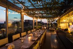 an outdoor dining area with wooden tables and chairs, lights strung from the ceiling, and large windows