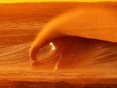 a large wave is coming in to the shore at sunset or sunrise, as seen from behind