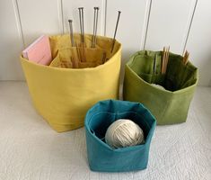 three different colored baskets with knitting needles in them