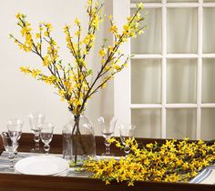 yellow flowers are in vases on a table set with glasses and placemats