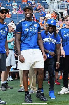 two men in blue shirts and white shorts are standing on the sidelines at a football game