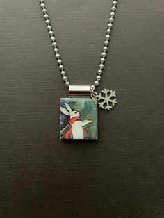 a necklace with a snowflake on it and a small square pendant hanging from the front