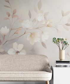 a white couch sitting in front of a wall with flowers on it and a potted plant next to it