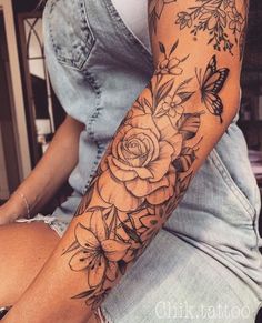 a woman's arm with flowers and butterflies tattooed on the arm, while sitting down