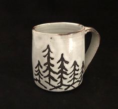 a white and black mug with trees painted on it