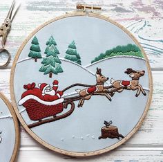 two embroidery hoops with santa's sleigh and reindeer on them, one being pulled by a dog