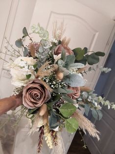 a woman holding a bouquet of flowers and greenery in front of a white door