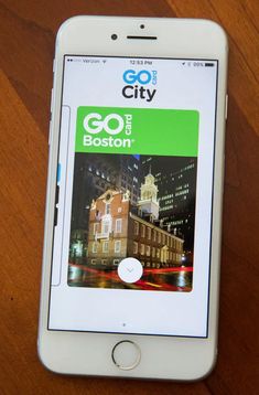 an iphone with the go boston app displayed on it's screen, sitting on a wooden table