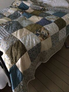 an unmade bed with a quilt on it in a room next to a window