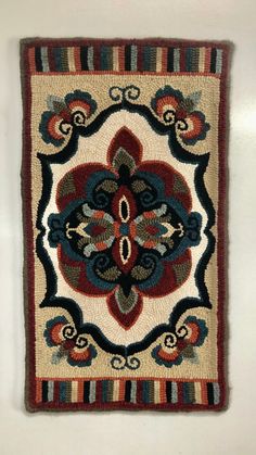 a square rug with an intricate design on the front and back side, hanging from a wall