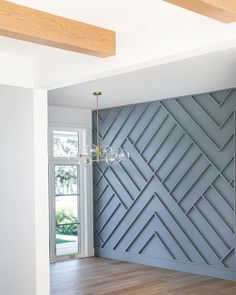 an empty room with wood flooring and blue wall paneling in the center, next to a chandelier