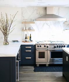 a kitchen with marble counter tops and stainless steel stove top oven, range hood, and open shelving