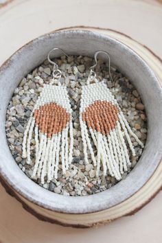 two white and orange beaded earrings sitting in a bowl on top of some rocks