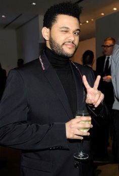 a man in a suit holding a drink and making the peace sign with his hand