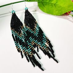 black and blue seed beaded earrings hanging from a green leafy plant on a white surface