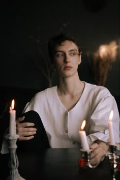 a young man sitting at a table with candles in front of him and one candle lit