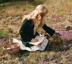 a woman sitting on the ground with a book in her lap and flowers around her