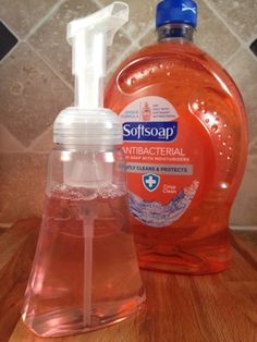 a bottle of soap sitting on top of a wooden table next to a glass container