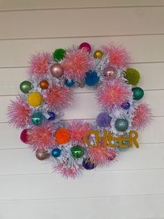 a christmas wreath with ornaments hanging on the side of a wall next to a sign that says cheer