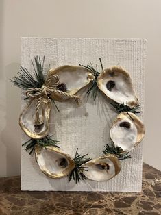 an oyster shell wreath is displayed on a white board with pine needles and evergreens