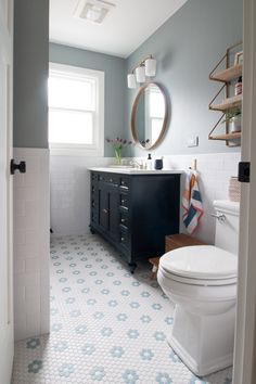 a white toilet sitting next to a sink in a bathroom under a round mirror on a wall