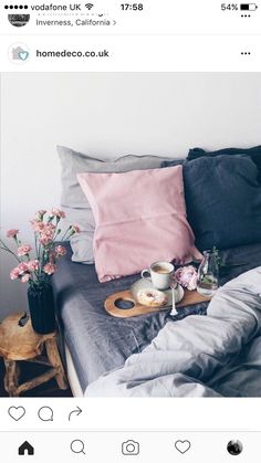 a bed with pink and grey pillows, coffee mugs and flowers on it