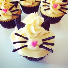 several cupcakes with white frosting and black cat ears on them, all decorated in yellow icing