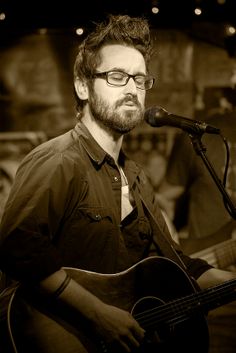 a man with glasses playing a guitar in front of a microphone