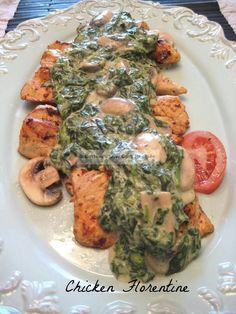 a white plate topped with chicken covered in spinach sauce and sliced tomato wedges