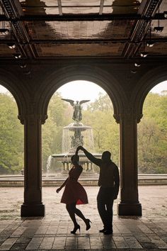 a man and woman dancing in front of a fountain