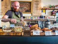 a man in an apron is behind a counter with bread and pastries on it