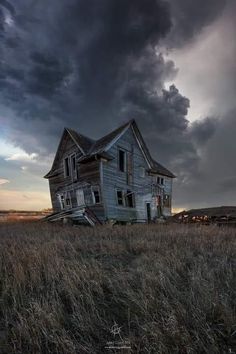 an old abandoned house in the middle of a grassy field under a dark sky with storm clouds