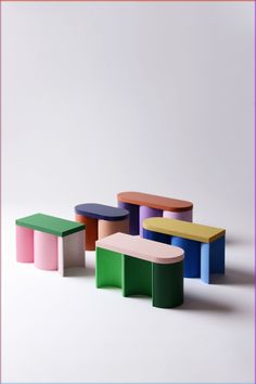 four different colored stools sitting next to each other on a white surface in front of a pink frame