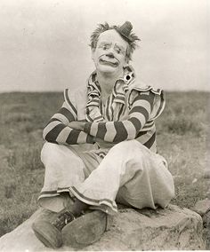 an old photo of a clown sitting on a rock