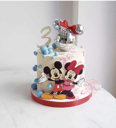 a birthday cake decorated with mickey mouse and minnie mouse on the top is a silver disco ball