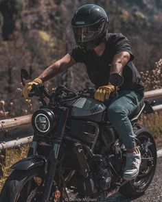 a man riding on the back of a motorcycle down a road next to a forest