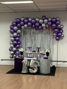 purple and silver balloons are on display in front of a table with chairs, vases and other decorations