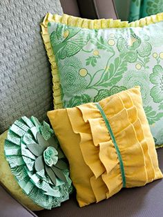 three pillows are sitting on a couch with green and yellow accents, one has a ruffled flower